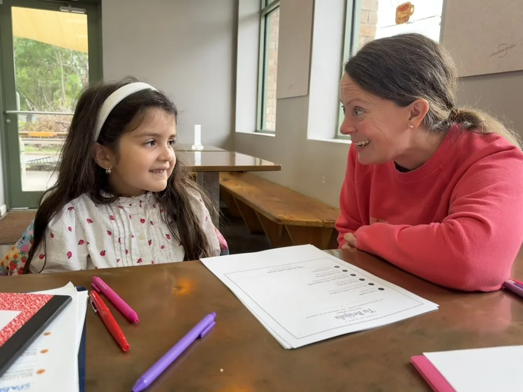 A mentor leans in, talking with a smiling young student across a worktable at Chispitas Studio.