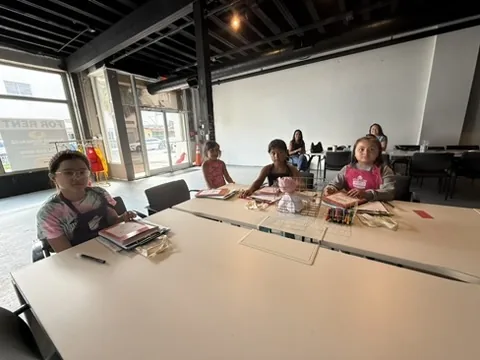Young students look up and smile from their seats around the worktable.